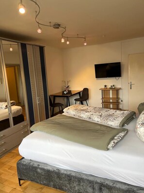 A bedroom with a bed, bedside tables, a desk, a chair, a TV, and a mirror. - Einzimmerwohnung in Innsbruck (Innsbruck)