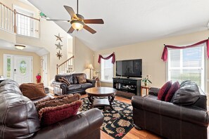 A spacious living room with leather sofas, a coffee table, a television, and a ceiling fan.