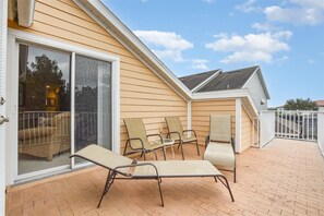 A covered patio with four chairs and a table, a sliding glass door, and a brick floor.