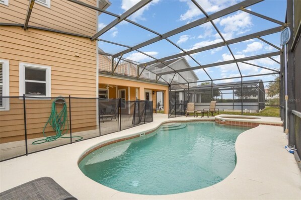 A covered outdoor swimming pool with a curved design, surrounded by a fence and a house.