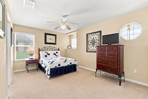 A bedroom with a bed, dresser, ceiling fan, and artwork on the walls.