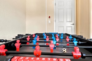 A foosball table with red and blue figures, a soccer ball, and a door in the background.
