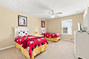 Quarto com duas camas, ventoinha no teto, janela com persianas e cômoda.