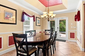 A dining area with a round table, chairs, a chandelier, and framed pictures on the walls.