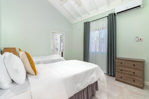A hotel room with two beds, a wooden dresser, an air conditioning unit, and a window with curtains. - Lot 9 Fairway (St. Ann's Bay)