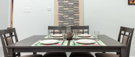 A dining area with a rectangular table set for four, surrounded by four chairs.