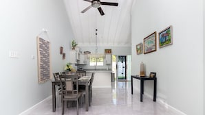 Un comedor espacioso con techos altos y un ventilador de techo, que da acceso a una cocina y vistas al exterior.