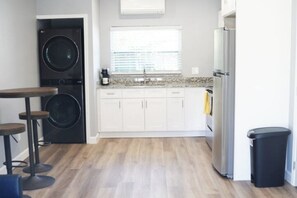 A compact kitchen with a washing machine, a small dining area, and a trash bin. - Eclectic 1 Bedroom Apt in Downtown Orlando. 15mins from Airport & UCF. (Orlando)