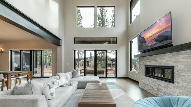 Uma sala de estar espaçosa com um amplo sofá de canto, uma televisão de tela plana acima de uma lareira e vista para o exterior por meio de grandes portas de vidro deslizantes.