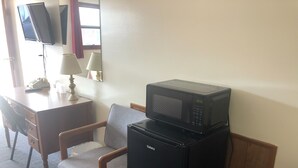 A hotel room with a desk, chair, and a microwave on a small refrigerator. - Dav-Ed Motel (Kingsville)