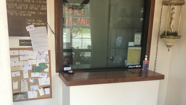 A reception desk with a clock, a bulletin board with notes, a trash can, and a "VACANCY" sign. - Dav-Ed Motel (Kingsville)