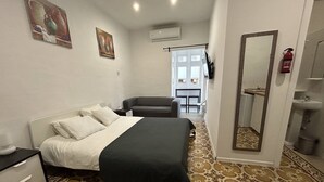 Une chambre à coucher comprenant un lit, une table de chevet, une chaise, un miroir, ainsi qu’une salle de bain avec un lavabo et des toilettes.