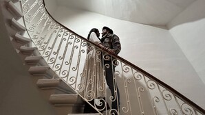 Un escalier en colimaçon orné de rampes en métal travaillées, et une personne qui le descend.