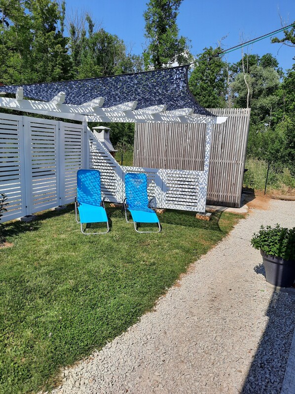 A patio area with two blue lounge chairs, a white pergola, and a wooden fence.