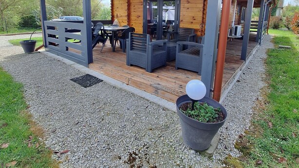 A covered outdoor seating area with tables and chairs, a wooden deck, and a gravel path.
