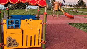 A playground with a red and yellow play structure, a slide, and a swing set.