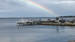 En lystbådehavn med både fortøjet ved træpillioner, en klar himmel og en regnbue i det fjerne.