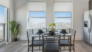Une cuisine moderne avec une table à manger pour quatre personnes, de grandes fenêtres et un réfrigérateur.