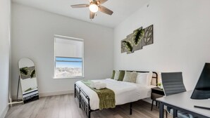 Une chambre à coucher comprenant un lit, un bureau, une chaise, un ventilateur de plafond, une fenêtre et des œuvres d’art accrochées au mur.