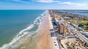 An aerial view of a coastal city with a beach, buildings, and a bridge.