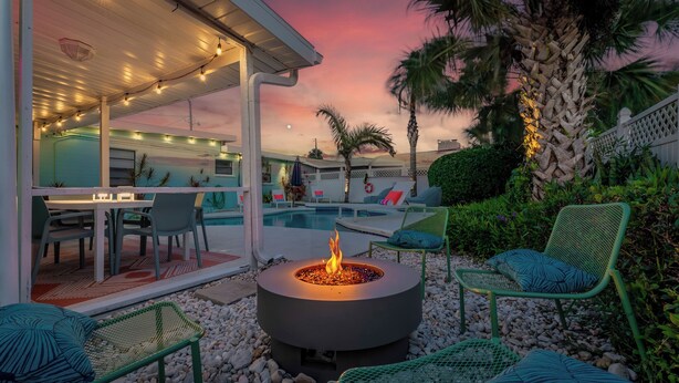 An outdoor patio with a fire pit, seating, and a pool in the background.
