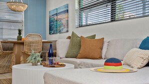 A modern living room with a sofa, a round coffee table, and a wicker chair. There is a small plant on the table and a colorful hat on the sofa.