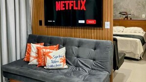 A modern living room with a grey sofa, a mounted TV displaying the Netflix logo, and a wooden panel wall. - Makia Beach Resort Experience Exclusive (Ipojuca)