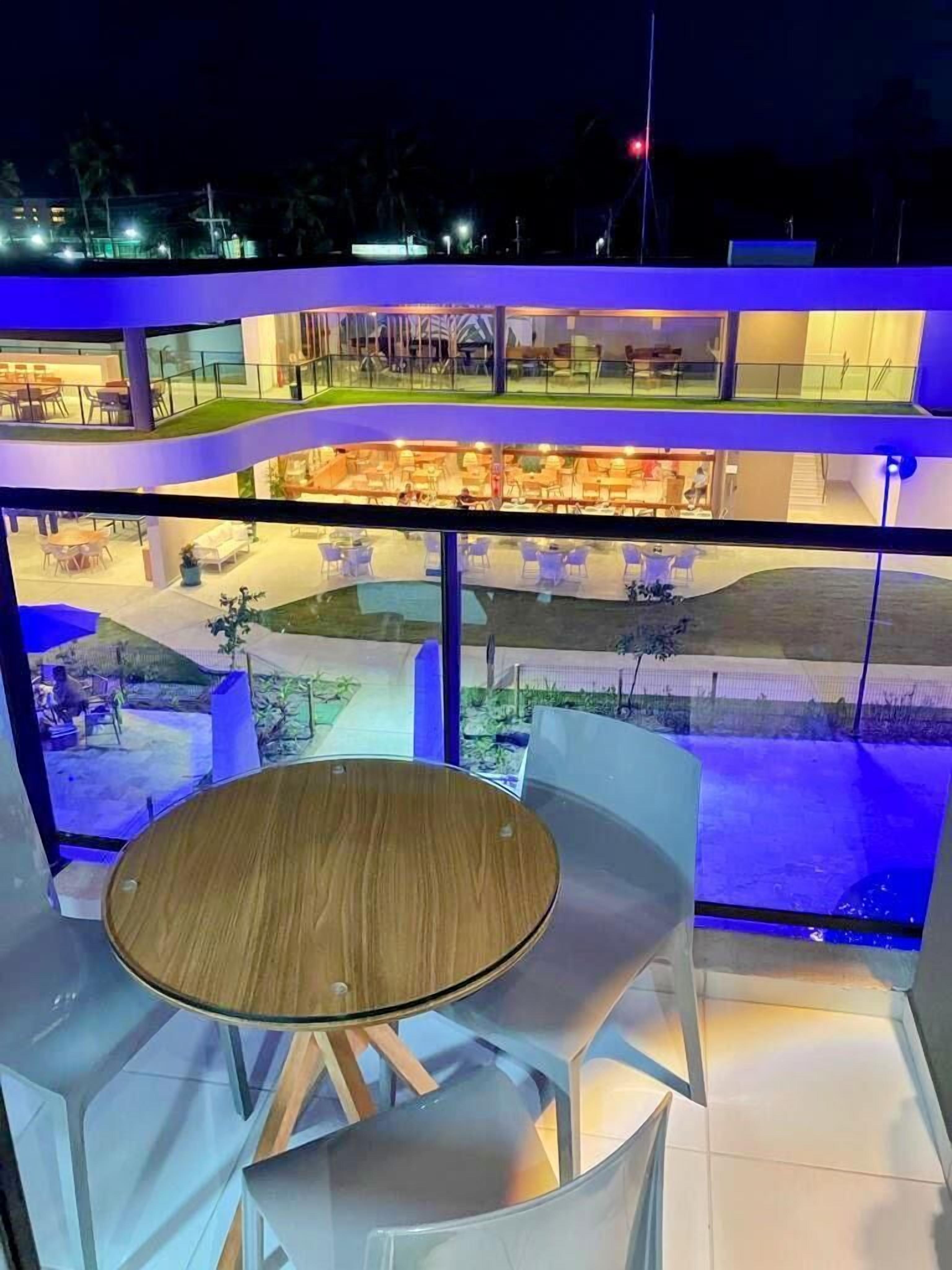 Un área de estar al aire libre, moderna, con una mesa redonda y sillas blancas, con vistas a un paisaje urbano iluminado por la noche.