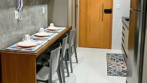A compact kitchen with a wooden table set for four, a refrigerator, and a door leading to another room. - Makia Beach Resort Experience Exclusive (Ipojuca)