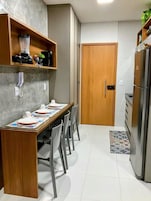 Cocina compacta con una mesa de madera dispuesta para cuatro personas, un refrigerador y una puerta que conduce a otra habitación.