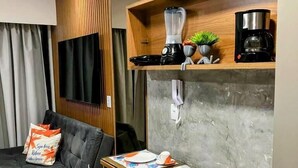 A modern living room with a grey sofa, a wooden dining table set for two, and a built-in shelf with a blender and coffee maker. - Makia Beach Resort Experience Exclusive (Ipojuca)
