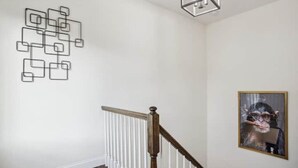 Una escalera con barandilla de madera y balaustres blancos, una obra de arte geométrica en la pared, y un cuadro enmarcado.