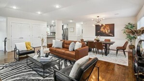 Una sala de estar moderna con un sofá marrón, alfombra blanco y negro, y un comedor con mesa y sillas.