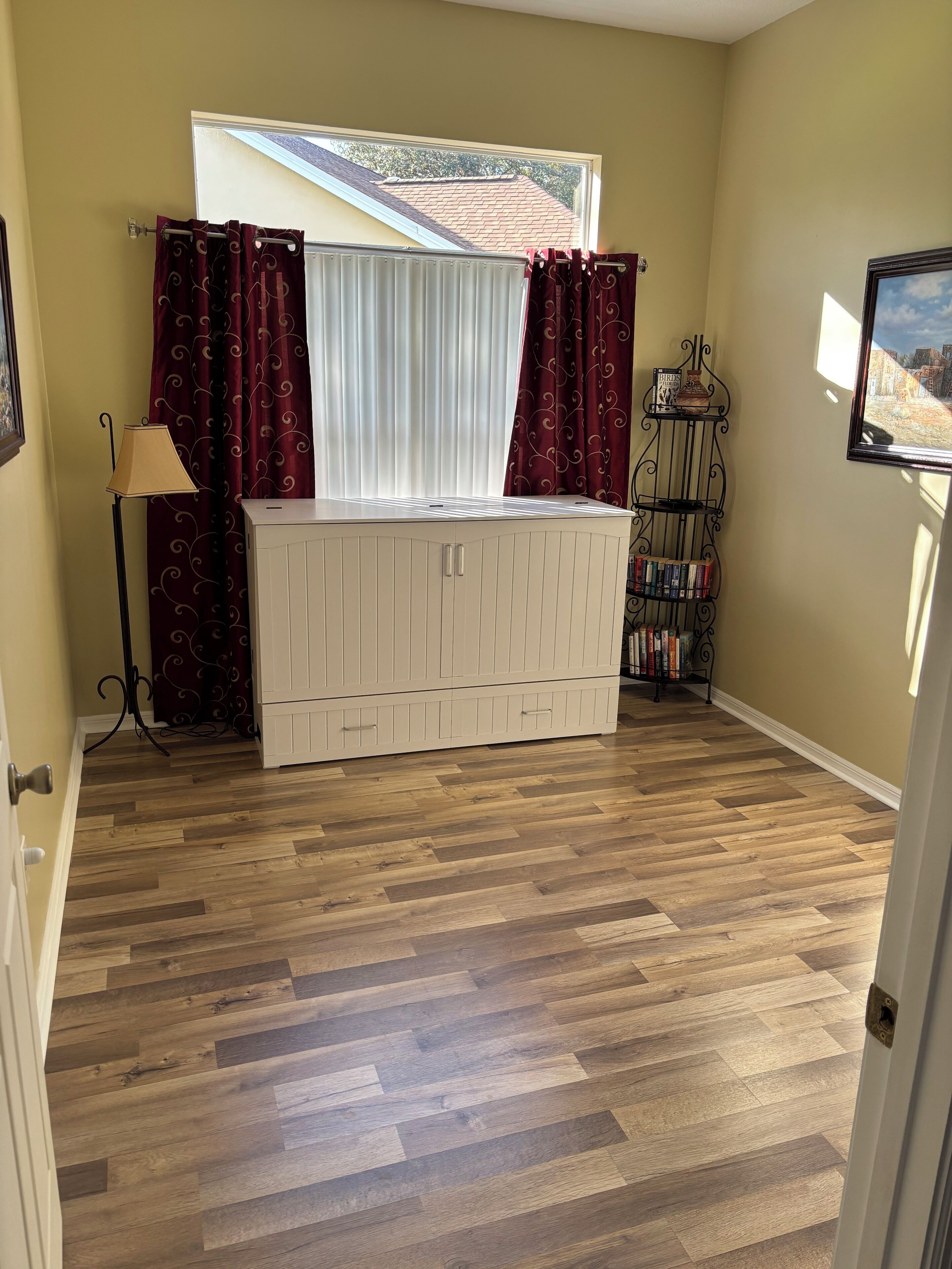 A room with a window, a radiator, a lamp, a bookshelf, and a door.