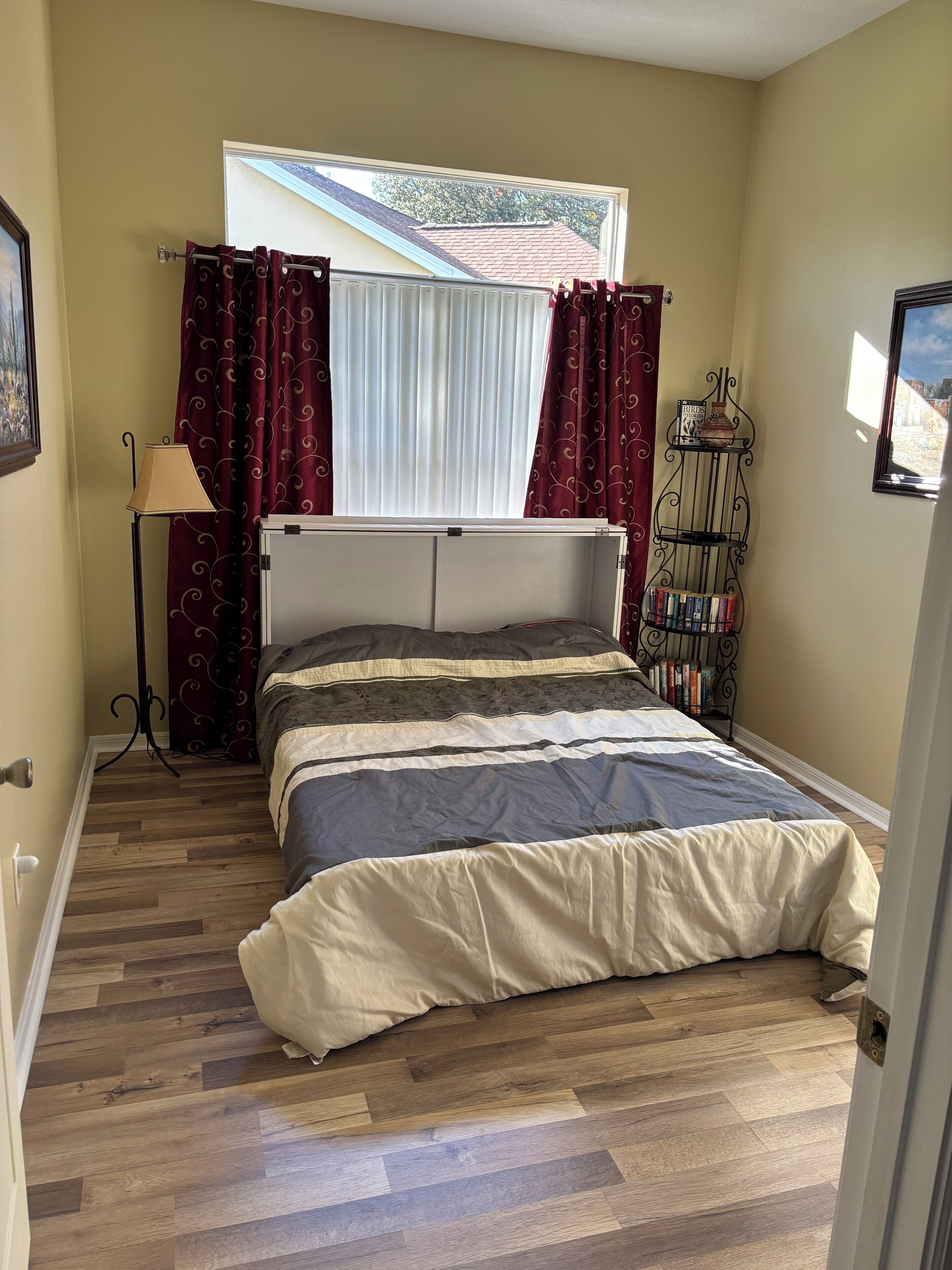 A bedroom with a bed, curtains, a lamp, and a bookshelf.