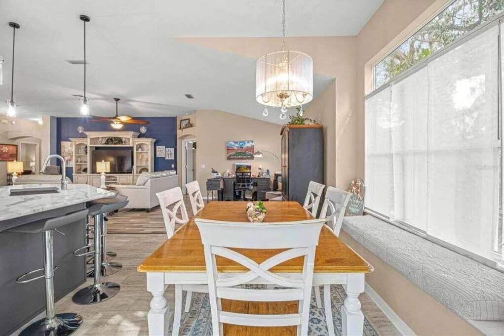 A modern kitchen with a dining area, featuring a wooden table, white chairs, and a chandelier.
