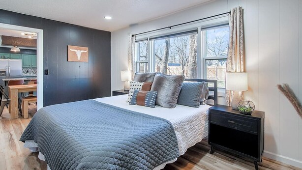 A modern bedroom with a large bed, a desk, and a window with curtains. - The Den is a cozy and welcoming 3 bed, 2 bath home with zero entry design (Wichita)