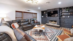 A modern living room with a leather sofa, a fireplace, and a television. - The Den is a cozy and welcoming 3 bed, 2 bath home with zero entry design (Wichita)