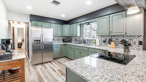 A modern kitchen with green cabinets, a stainless steel refrigerator, a microwave, and a granite countertop. - The Den is a cozy and welcoming 3 bed, 2 bath home with zero entry design (Wichita)