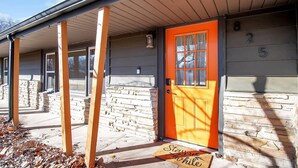 A house with a stone facade, a bright orange door, and a covered porch. - The Den is a cozy and welcoming 3 bed, 2 bath home with zero entry design (Wichita)