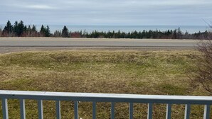 A grassy area with a road and trees in the background. - Charming rustic retreat with Bay of Fundy Views, escape to our serene haven. (Hampton)