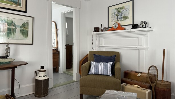 A cozy living room with a green armchair, a fireplace, and vintage suitcases. - Charming rustic retreat with Bay of Fundy Views, escape to our serene haven. (Hampton)