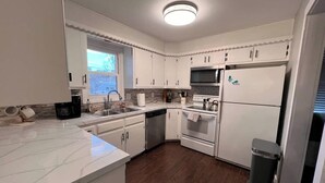 Una cocina moderna con armarios blancos, un lavamanos de acero inoxidable, un horno empotrado y un refrigerador.