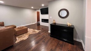 Un salón amplio con un sofá de cuero marrón, un mueble multimedia negro y una alfombra grande sobre el suelo de madera.