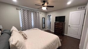 Un dormitorio con cama, cómoda, televisor y ventilador de techo.