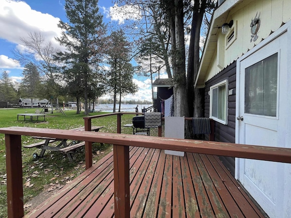 A wooden deck with a railing, a grill, and a view of a lake and cabins.