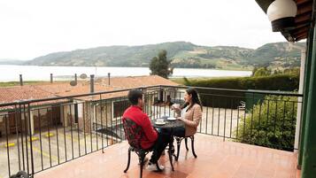 A balcony with a view of a lake and hills, featuring a table and chairs.