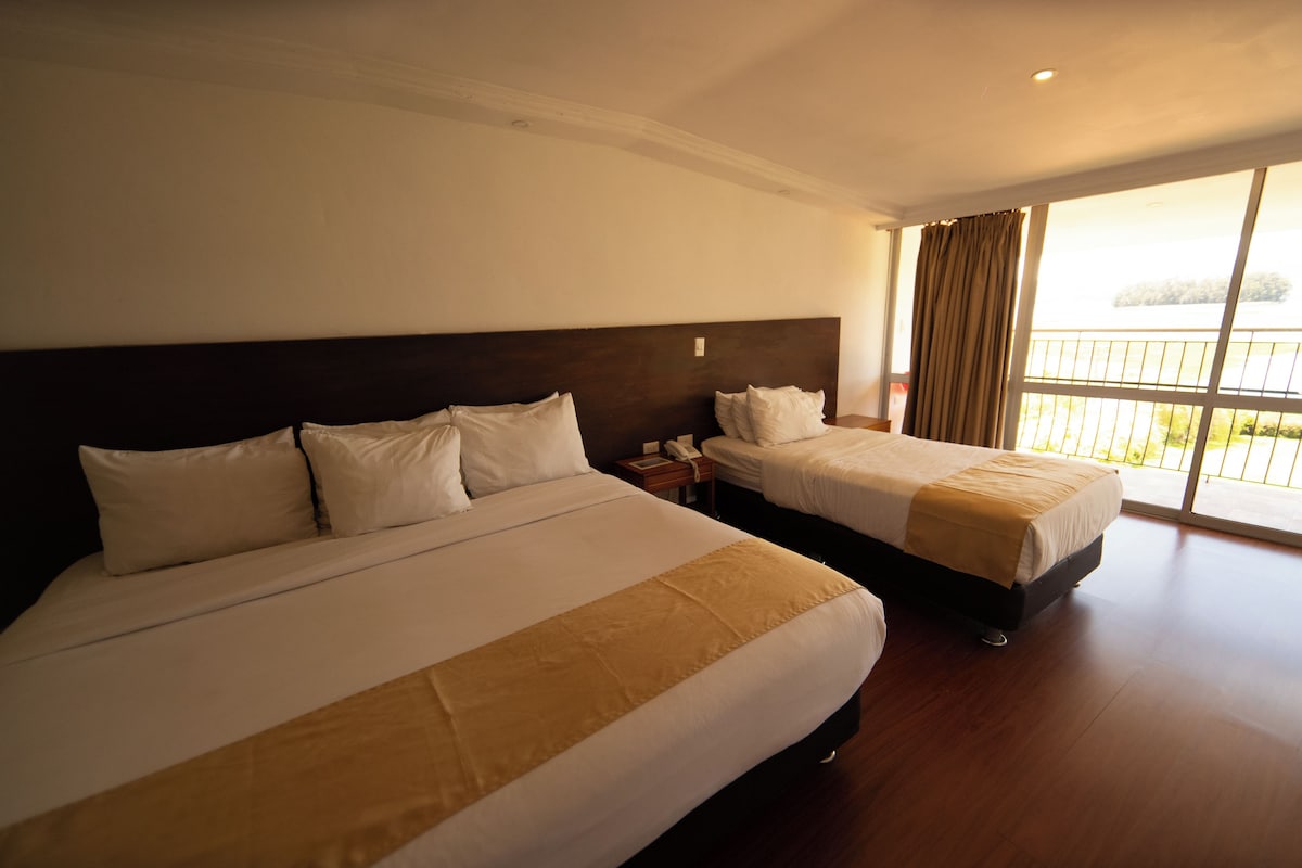 Habitación de hotel con dos camas, una mesita de noche y un ventanal con vistas.