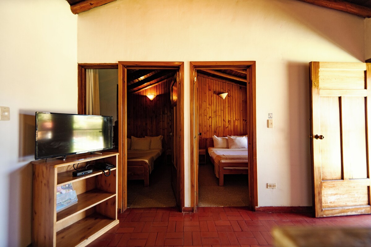 Un interior de madera con un televisor sobre una estantería, una cama con almohadas y una puerta que da a otra habitación.