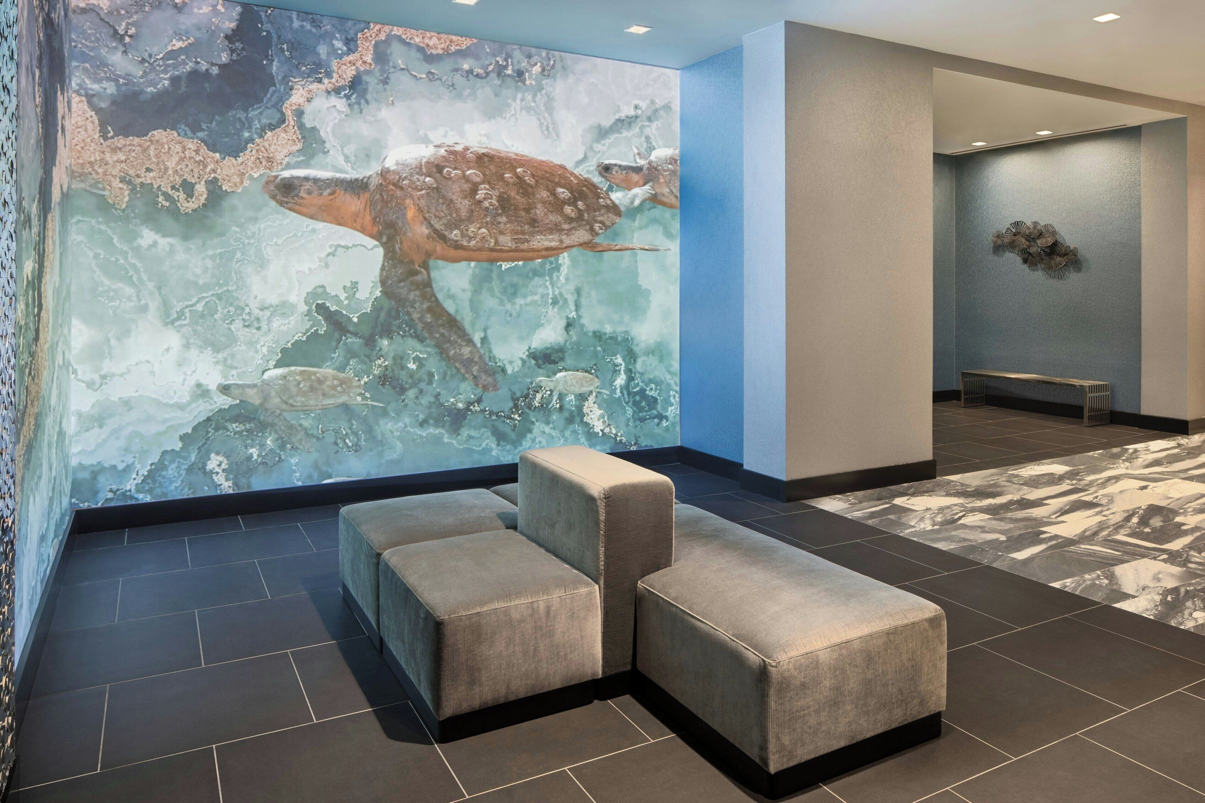 A lobby with a large mural of a sea turtle, a seating area with cushioned benches, and a patterned floor.